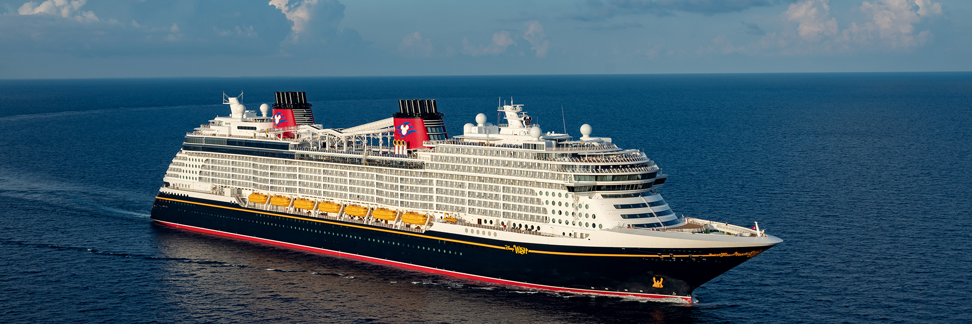 Cruise ship traveling across open water under a bright blue sky with scattered clouds.