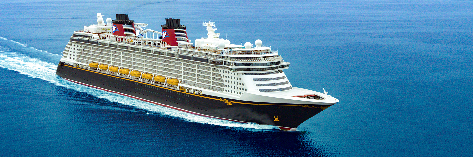 Large cruise ship sailing across deep blue water with a mountainous coastline in the background.