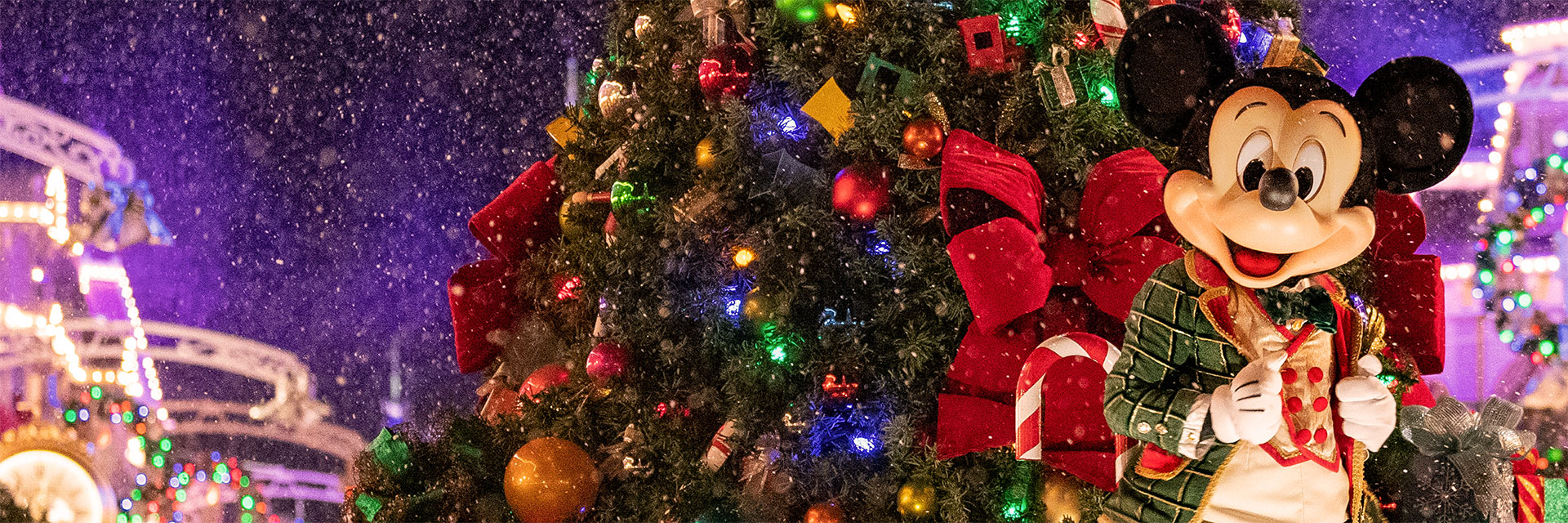 Mickey dressed in holiday clothes in front of a Christmas tree.